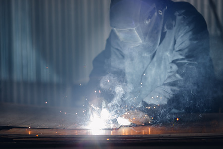 Professional welder in protective uniform with face mask, sparks fly apart, welding with an electrode.の写真素材