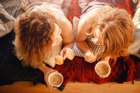 Girlfriends young women woke up in bedroom and drink morning coffee with croissant. Concept guests pajama party.の写真素材