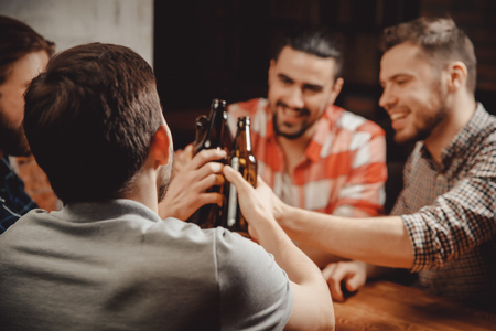 Four bearded young men old friend celebrating, celebrate narrow range in Brasserie, drinking craft beer beverages from bottles, talking toastの写真素材
