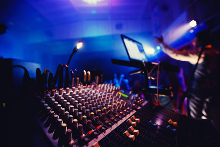 Sound equipment in nightclub party. DJ console, people dancing in background, around bright lights.