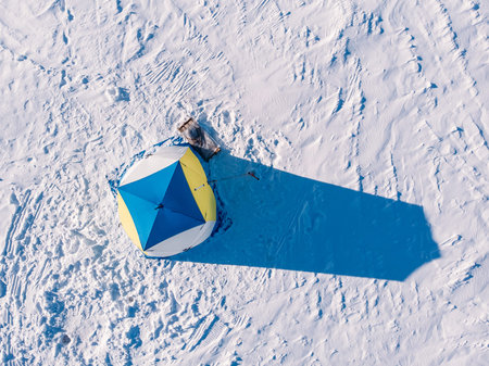 Tent for winter ice fishing, top aerial view, fisherman holding rod in hole lake.の写真素材