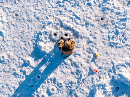 Winter fishing on ice, top aerial view, fisherman rod in hole in lake.の写真素材
