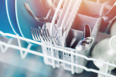 Open dishwasher with clean shine dishes and forks, spoons, cutlery. Concept water saving. Top viewの写真素材