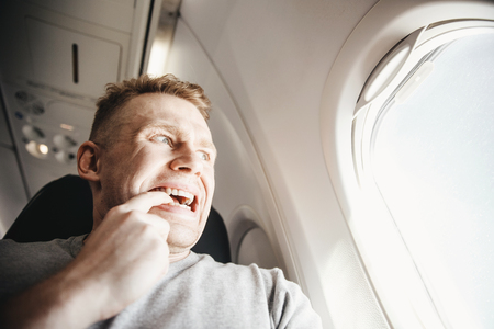 Male passenger in plane screams and cries, aerophobia. background of porthole. Concept fear of flying on airplane.の写真素材