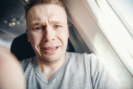 Passenger man in plane clutches his head, afraid of heights and flight. Scream and cry expression.の写真素材