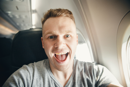 Happy tourist man makes selfie photo in cabin aircraft airplane before departure. Travel concept.の写真素材