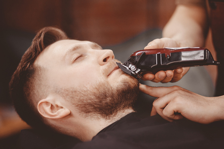 Barber cuts his beard to man in armchair.の写真素材