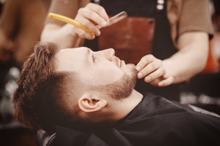Man Barber shaves beard of client on chair Barbershop.の写真素材