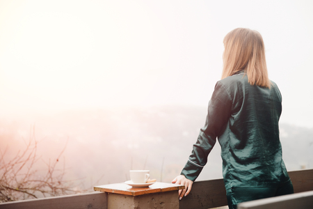 Beautiful young woman with cup coffee on terrace in green pajamas meets morning.の写真素材