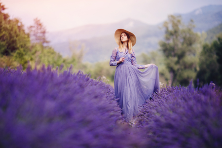 Beautiful girl in long purple dress walks among lavender fields, France, Provence. Foreground and background with mountains blurredの写真素材