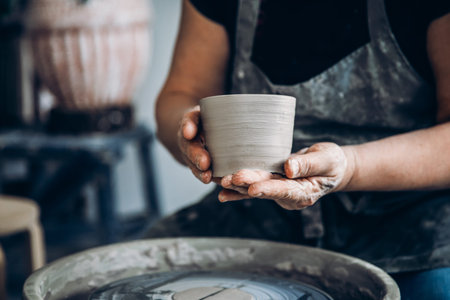 Master holds pot made of clay on potter wheel.