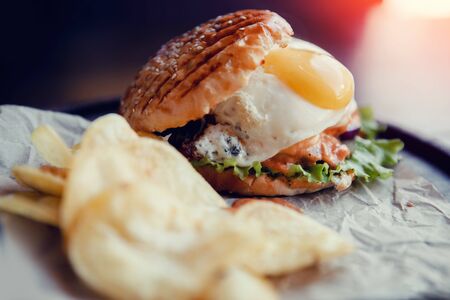 Appetizing burger with fried egg, meat patty, grilled bun. Near potato chips. Concept fast food.の写真素材