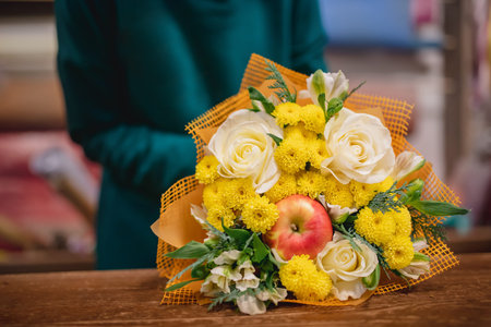 Florist makes autumn bouquet of roses flowers, apples red, green and yellow leaves.