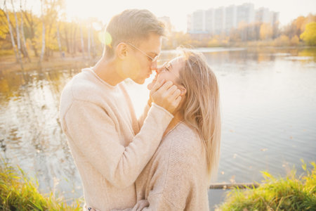 Loving couple in sunglasses round shape cuddle sweater and kiss against backdrop of autumn park.