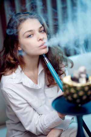 Young beautiful woman in night club smoke hookah or shisha bar, blue background
