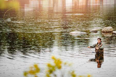 Fisherman using rod fly fishing in mountain river autumn splashing water.の写真素材