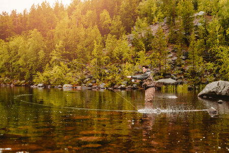 Fisherman using rod fly fishing in mountain river sunset.