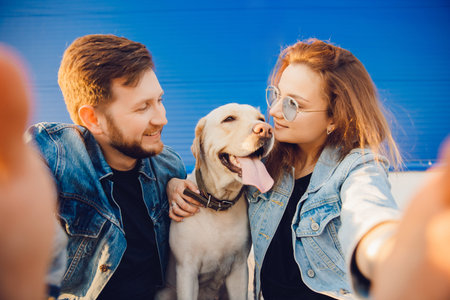 Lifestyle summer walk concept. Happy couple making selfie photo with new pet dog retriever Labrador...