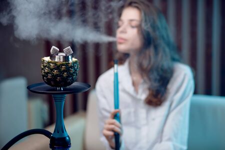 Young beautiful woman in night club smoke hookah or shisha bar, blue backgroundの写真素材
