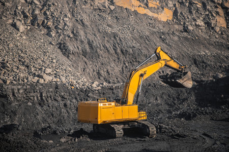 Large yellow excavator with full bucket of black coal will carry out loading in open mine.