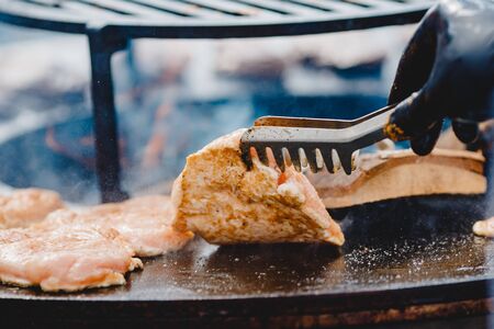 Cook grills steaks and pork ribs open fire. Turns meat over with tongs. Street food conceptの写真素材