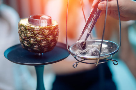 Hookahman changes coals for hookah with tweezers, bowl of pineapple blueの写真素材