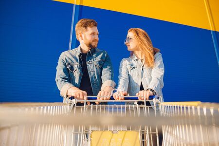 Young couple holding supermarket cart for groceries and heading towards store entranceの写真素材