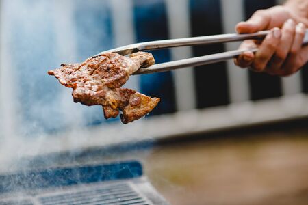 Cook grills steaks and pork ribs open fire. Turns meat over with tongs. Street food concept.の写真素材