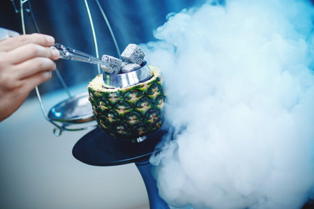 Hookahman changes coals for hookah with tweezers, bowl of pineapple blue