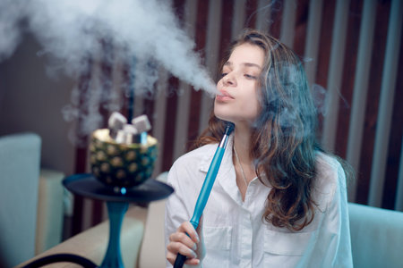 Young beautiful woman smokes hookah on tobacco with pineapple bowl