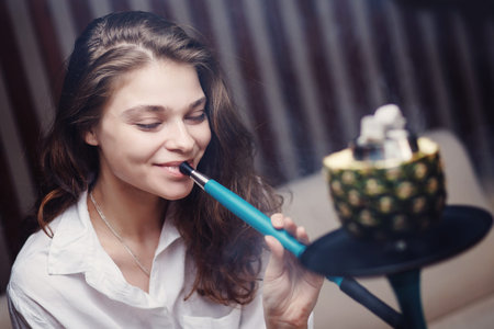 Young beautiful woman smokes hookah on tobacco with pineapple bowl