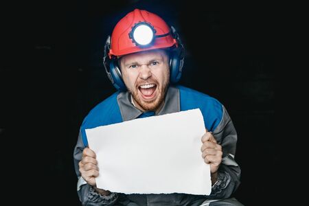 Miner angry man screams and frowns, holds sheet of paper for text. Concept mining strike uprisingの写真素材