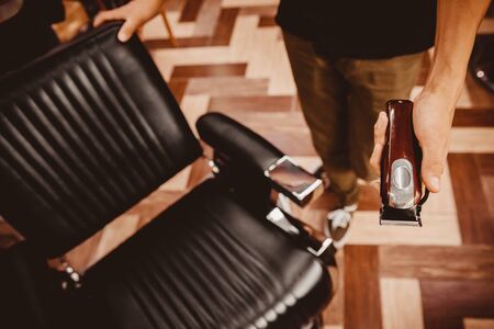 Barber hairdresser holds clipper on background chair, beauty salon for menの写真素材