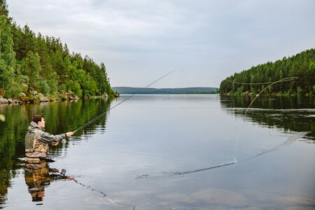 Fisherman using rod fly fishing in mountain river summer splashing waterの写真素材