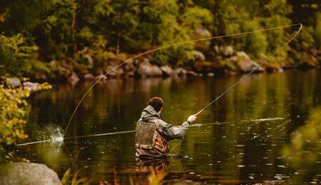 Fisherman using rod fly fishing in mountain riverの写真素材