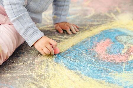 Child draws hand in colored chalk drawing on pavement. Top view.の写真素材