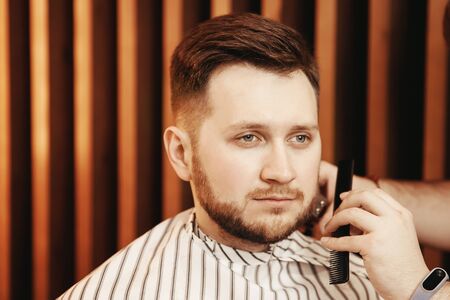 Barber shaves his beard to hipster man in barbershop. Toned photo, vintage styleの写真素材