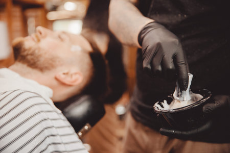 Brush for shaving beard along with bowl, blurred background of hair salon for men, barber shop.