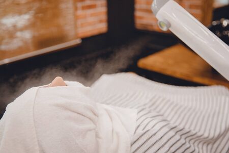 Man sits in barbershop chair and steam his face with hot towel in front of royal beard shaving razor.の写真素材
