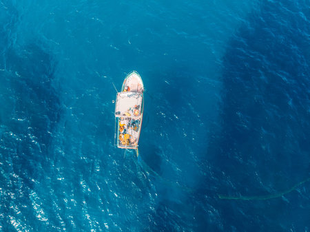 Fishing boat in blue sea water, fishermen set nets for fish. Aerial top view
