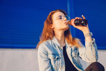 Moscow, Russia - June 27, 2019: Beautiful young woman happy drinking Coca Cola glass bottle soda in hand, sunsetのeditorial素材