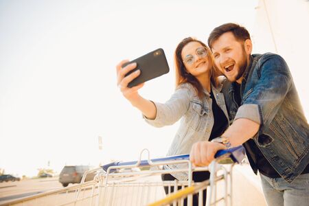 Happy young couple taking selfie photo on phone with trolley for supermarketの写真素材