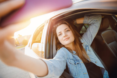 Concept travel trip. Beautiful girl driver makes selfie photo wheel of car