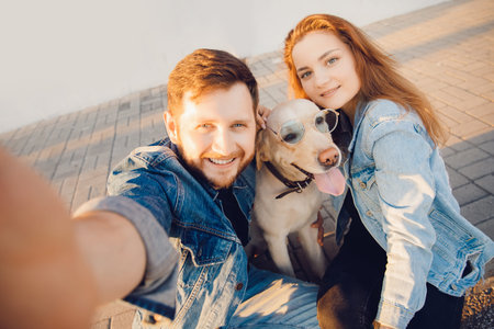 Happy couple making selfie photo with new pet dog retriever Labrador outdoors. Lifestyle summer walk...