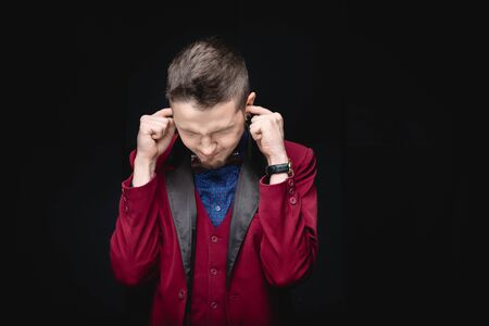 Man in red jacket covers ears with fingers, concept of lie, provocation, fatigue from peopleの写真素材