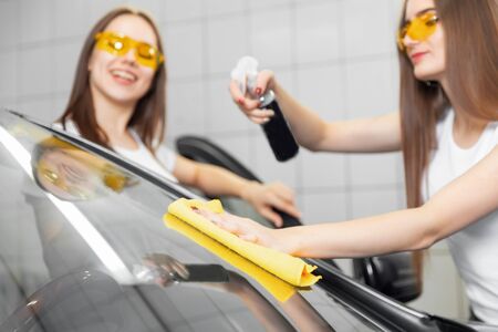 Two beautiful women worker washing windshield with sponge on car, window polishingの写真素材