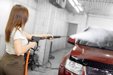 Car washing service. Worker woman cleaning auto using high pressure waterの写真素材