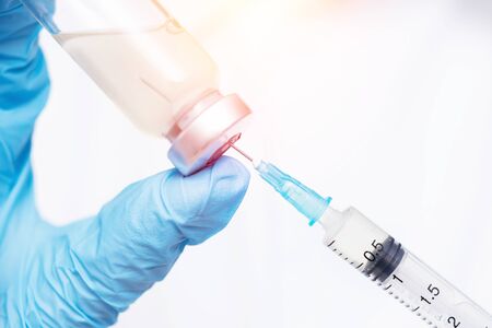 Doctor hand holding syringe and vaccine in blue gloves white coat, sun light. Concept disease injectionの写真素材