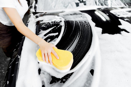 Background hand hold sponge over black car for washing white foam