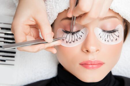Eyelash extension procedure. Master tweezers fake long lashes beautiful female eyesの写真素材